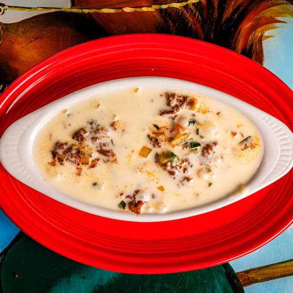 Queso Fundido, a creamy cheese dip with chorizo and peppers, served in a white dish on a red plate.