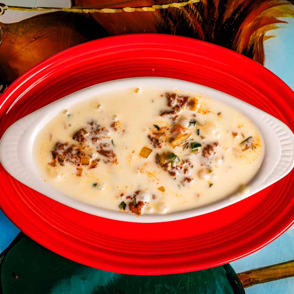 Queso Fundido, a creamy cheese dip with chorizo and peppers, served in a white dish on a red plate.
