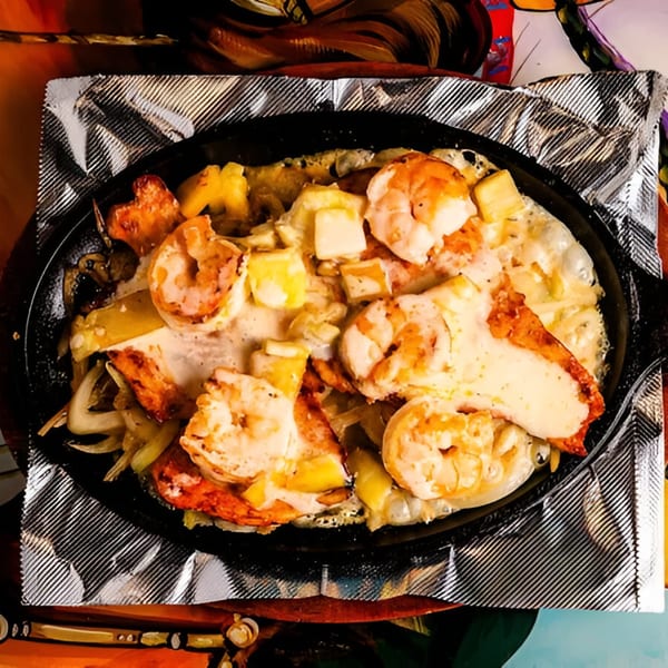 Sizzling shrimp fajitas with onions, peppers, and melted cheese in a black skillet.