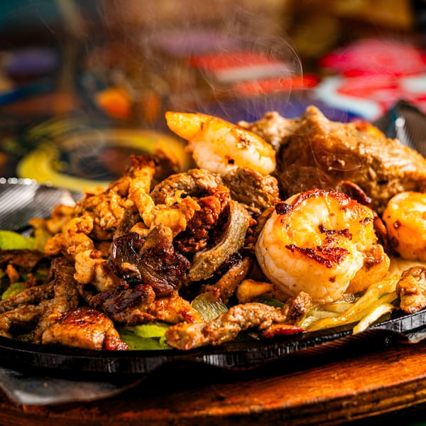 Sizzling Los Gallos Mexican Grill fajitas with steak, chicken, and shrimp, served on a hot plate.