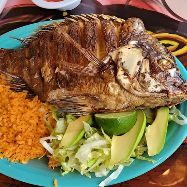 A whole fried fish with rice, shredded lettuce, avocado slices, and lime on a blue plate.