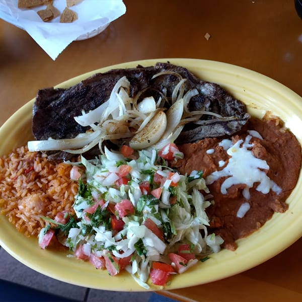 Carne asada with grilled onions, rice, refried beans, and pico de gallo on a yellow plate.