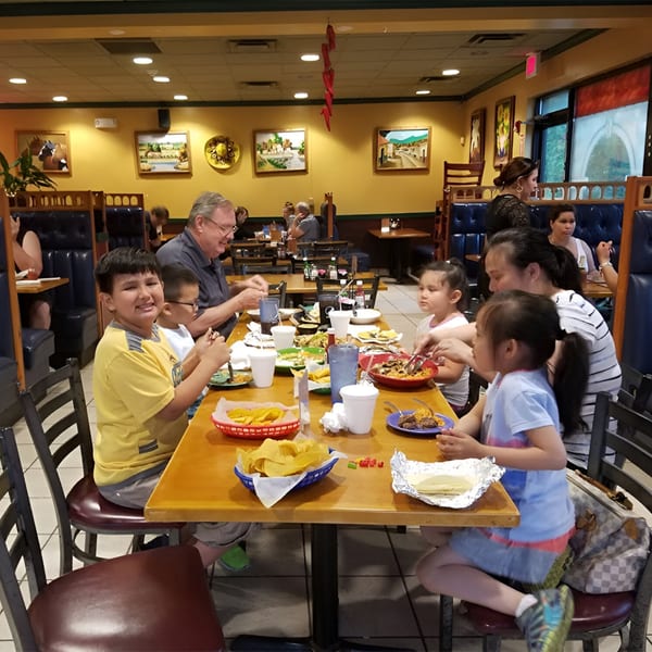 Families and children enjoy meals at tables in a vibrant, yellow-walled Los Gallos Mexican Grill dining room.