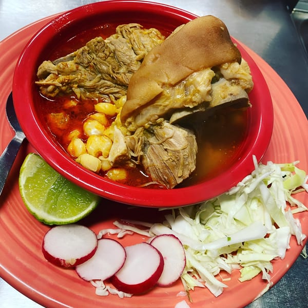 Pozole Rojo with pork, hominy, lime, radishes, and shredded cabbage on a red plate.