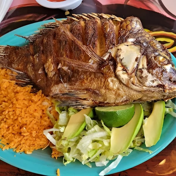 A whole fried fish with rice, shredded lettuce, avocado slices, and lime on a blue plate.