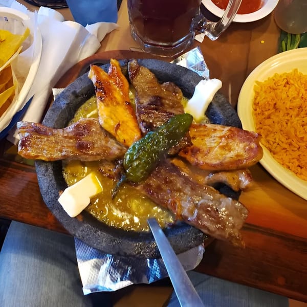 A sizzling molcajete with grilled meats, green sauce, and cheese, served with rice and chips.