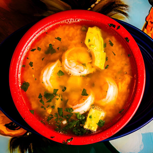 Top-down view of a vibrant red bowl filled with shrimp soup, avocado, and cilantro.