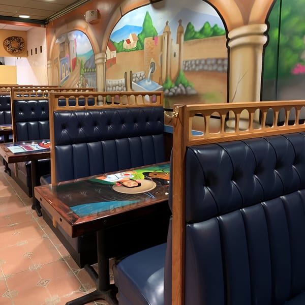 Los Gallos Mexican Grill interior with blue booths, wooden tables, and a vibrant mural of a Mexican village.
