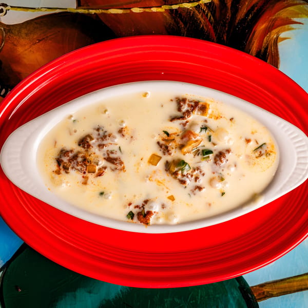 Creamy white queso dip with ground meat, diced peppers, and spices in a white dish on a red plate.