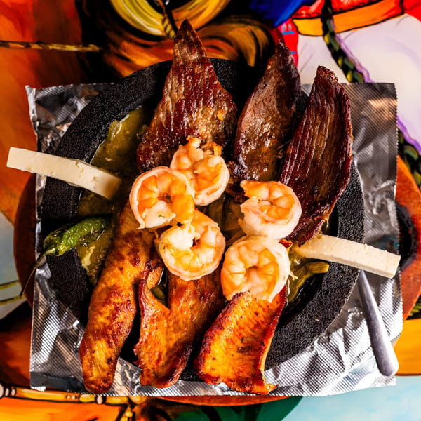 Molcajete with grilled steak, chicken, shrimp, cheese, and peppers in a green sauce.