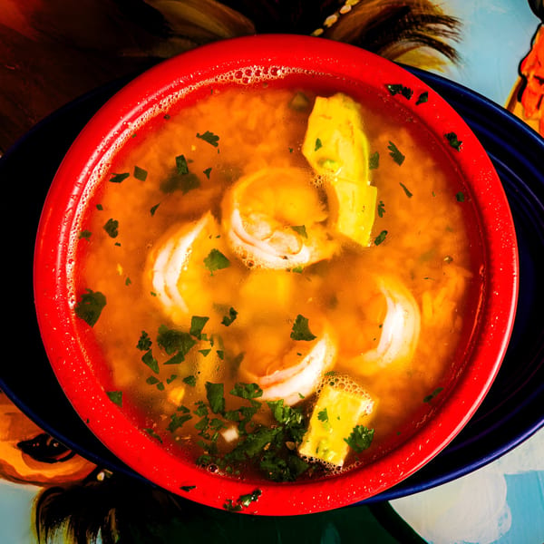 Top-down view of a vibrant red bowl filled with shrimp soup, garnished with cilantro and avocado.