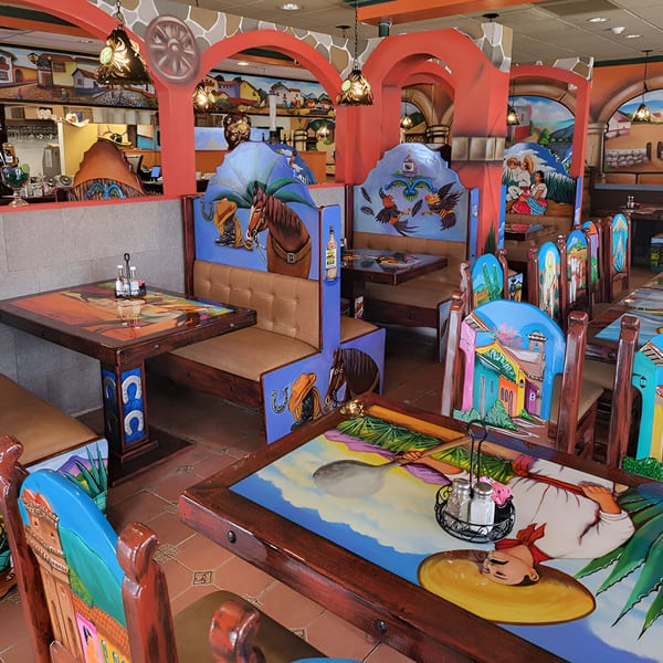 Vibrant, colorful Mexican restaurant interior with hand-painted tables, chairs, and booths featuring cultural scenes and motifs.